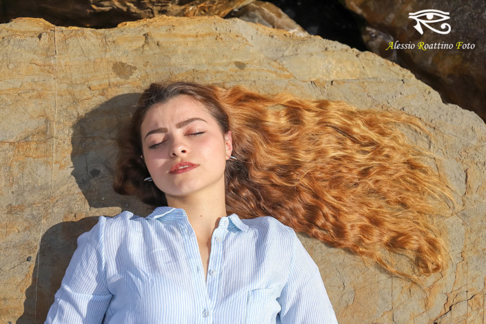 Adriana, ragazza ripresa in primo piano mentre è assopita sotto i raggi del sole con i capelli lunghi adagiati sullo scoglio a mo di bandiera
